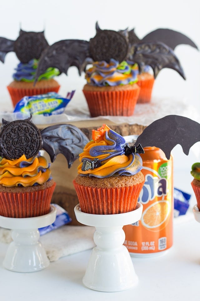 Oreo Crusted Orange Fanta Cupcakes - Adorable bat topped orange flavored cupcakes with a cute swirl of Halloween colored frosting! The cupcakes are also dipped in a orange Fanta glaze and crusted with Oreos for an extra touch.