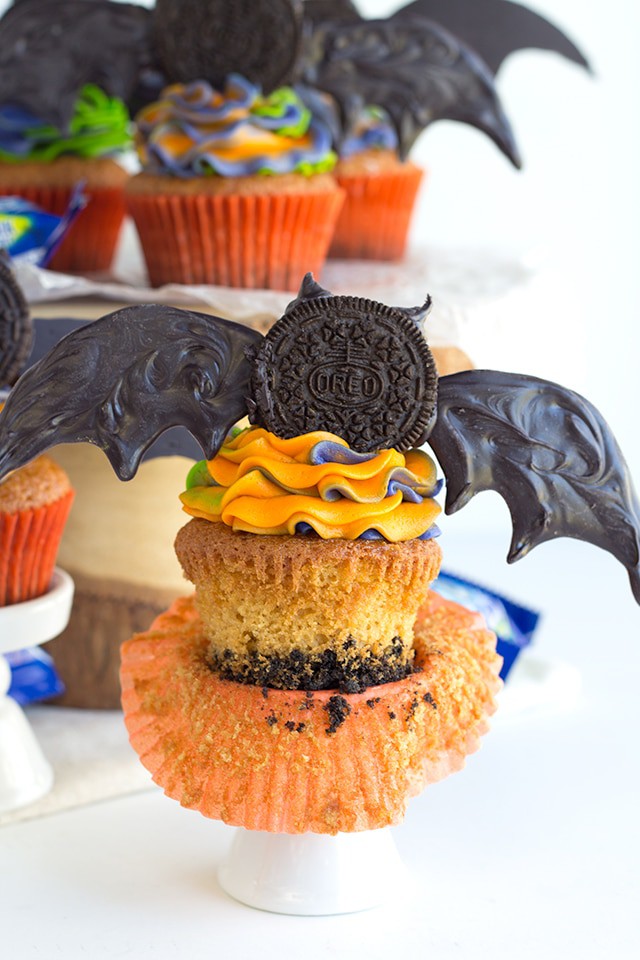 Oreo Crusted Orange Fanta Cupcakes - Adorable bat topped orange flavored cupcakes with a cute swirl of Halloween colored frosting! The cupcakes are also dipped in a orange Fanta glaze and crusted with Oreos for an extra touch.